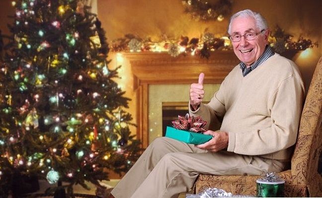 Дедушка возле новогодней елки с подарком
